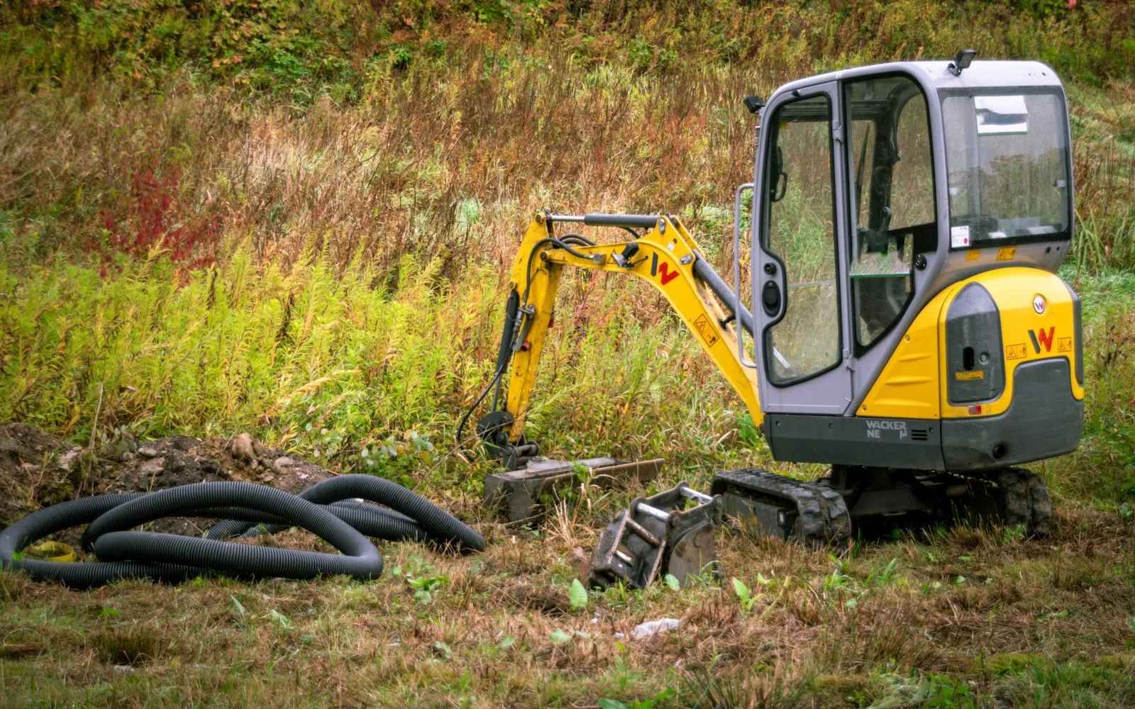 Mini excavator on grass with coiled hoses beside the tracks