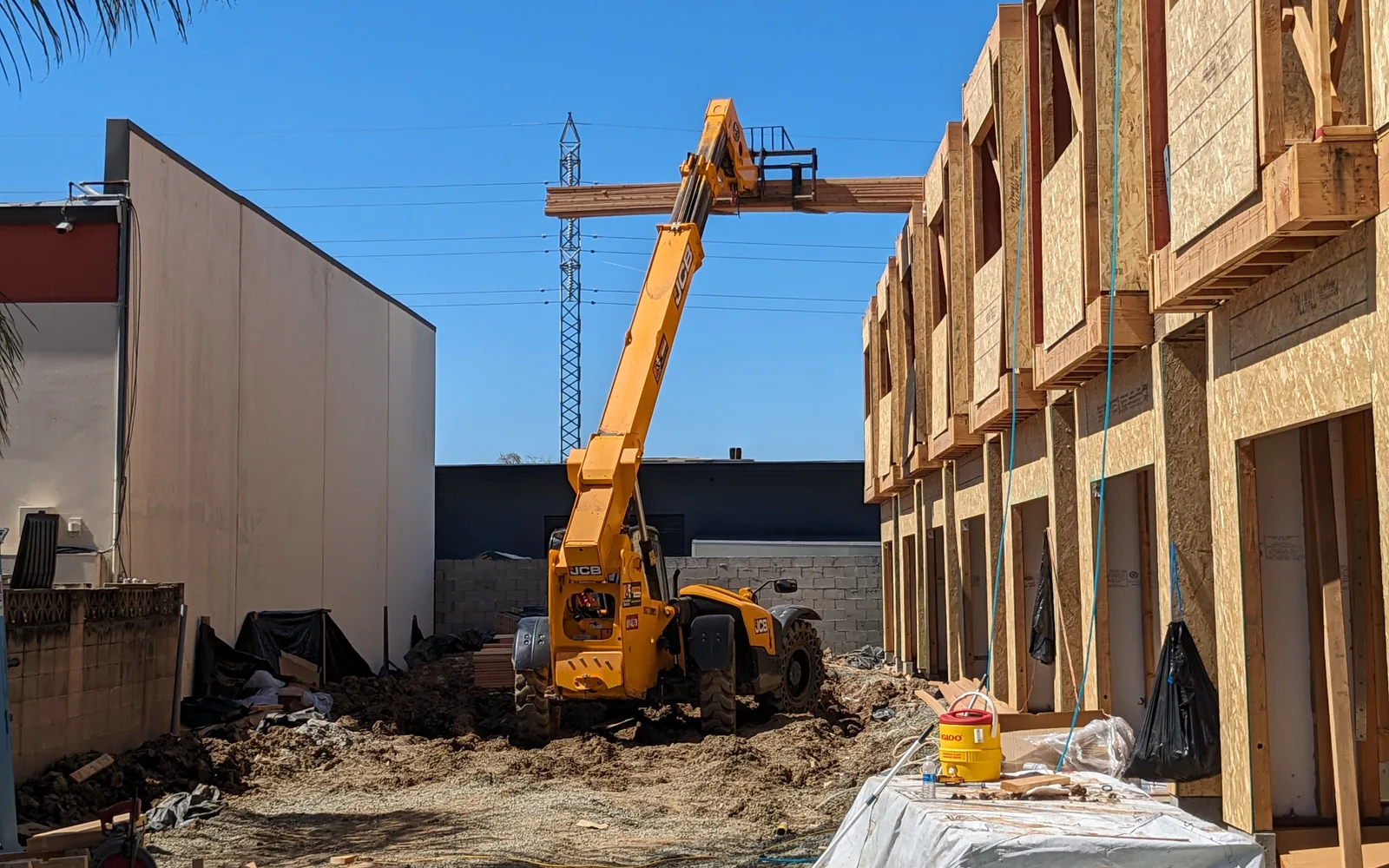 Telehandler placing a timber beam onto a framed building from a construction site